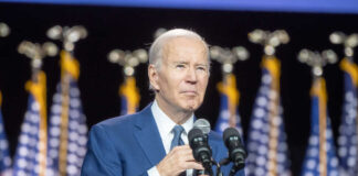 Man speaking at podium with American flags behind.